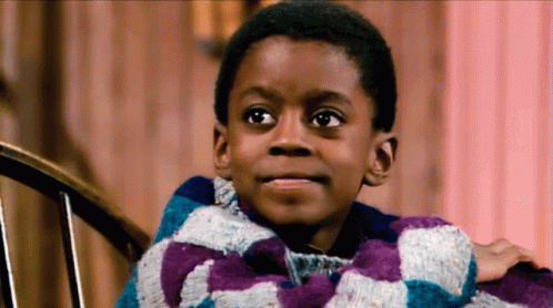 A Young Boy Is Sitting In A Chair Wearing A Purple And Blue Plaid Sweater GIF
