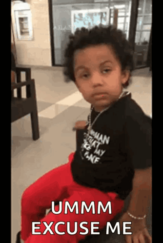 A Young Boy Is Sitting In A Chair With The Words Ummm Excuse Me Written On The Screen . GIF