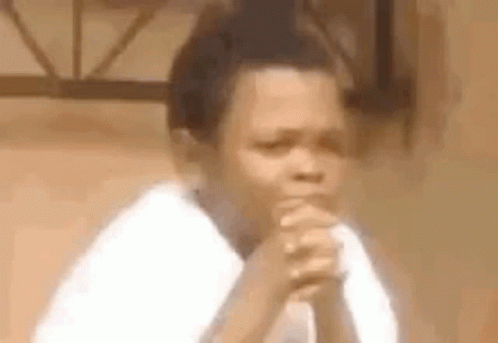 a young boy is sitting with his hands folded in prayer .