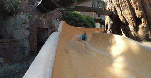 A Young Boy Is Sliding Down A Slide In Front Of A Tree GIF