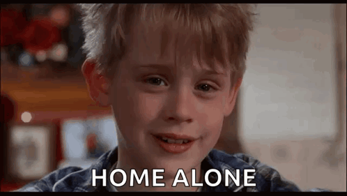 A Young Boy Is Smiling And Saying `` Home Alone '' While Looking At The Camera . GIF