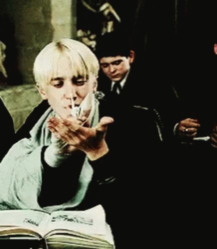 A Young Boy Is Smoking A Cigarette While Sitting In Front Of A Book GIF