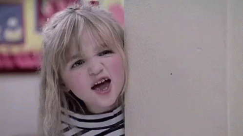 A Young Boy Is Standing In Front Of A Red Door Looking Out The Window . GIF