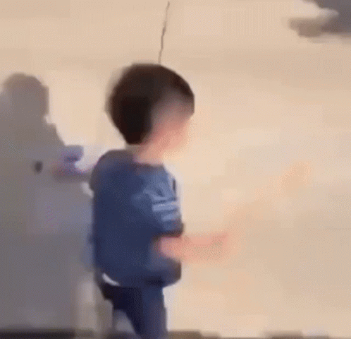 A Young Boy Is Standing In Front Of A Wall And Holding A Remote Control . GIF