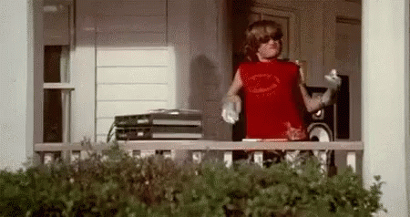 A Young Boy Is Standing On A Porch Wearing Sunglasses And A Red Tank Top . GIF