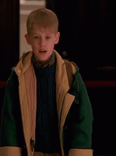 A Young Boy Is Wearing A Green And Yellow Jacket And A Blue Sweater . GIF