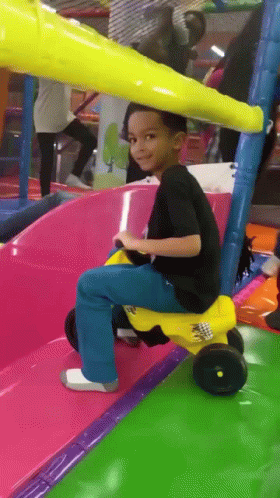 A Young Boy Riding A Yellow Toy Car On A Slide GIF