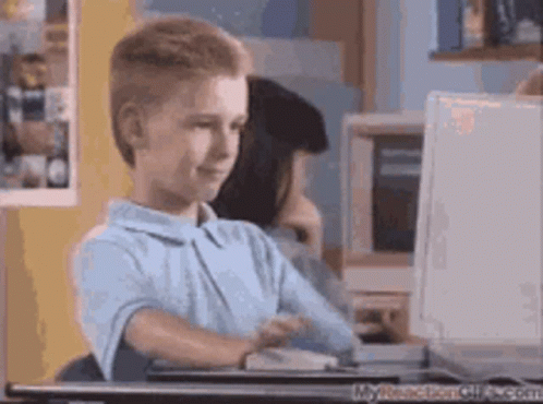 A Young Boy Sits At A Desk In Front Of A Computer GIF