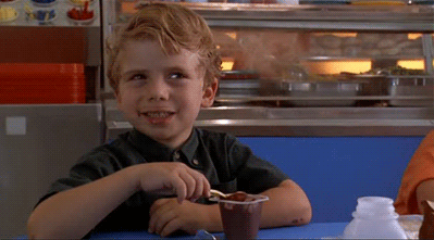 A Young Boy Sits At A Table With A Cup Of Chocolate Pudding GIF