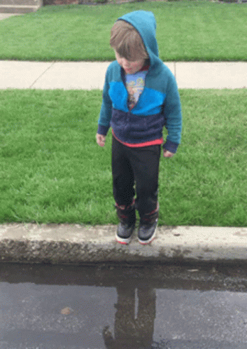 A Young Boy Standing In A Puddle With His Reflection In The Puddle GIF