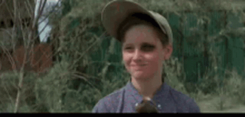 A Young Boy Wearing A Baseball Cap And A Blue Shirt Is Waving His Hand In The Air . GIF