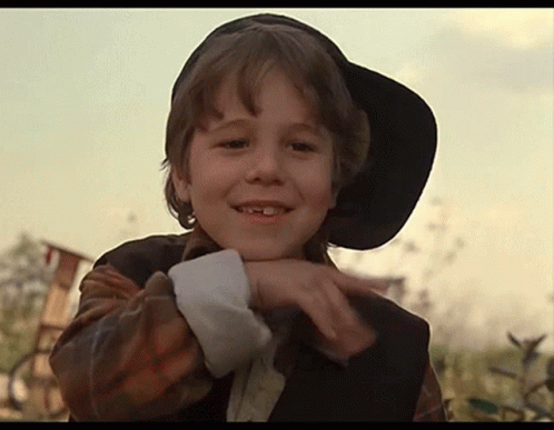 A Young Boy Wearing A Black Hat And A Plaid Shirt Is Smiling GIF