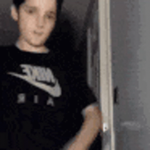 A Young Boy Wearing A Black Nike T-Shirt Is Standing In Front Of A Door . GIF