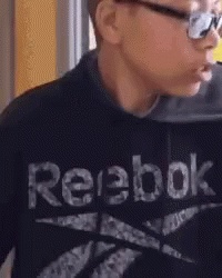 A Young Boy Wearing A Black Reebok Sweatshirt Is Eating Something . GIF