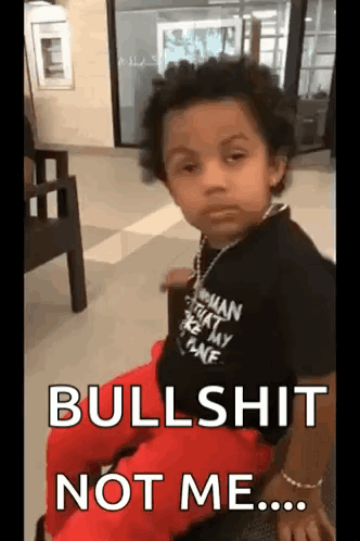 A Young Boy Wearing A Black Shirt And Red Pants Is Sitting In A Chair And Says `` Bullshit Not Me ... '' GIF