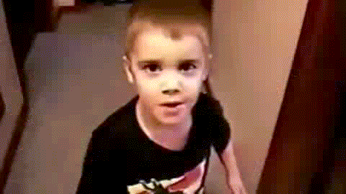 A Young Boy Wearing A Black Shirt Is Standing In A Hallway . GIF
