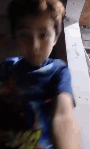 A Young Boy Wearing A Blue Shirt With The Word Spiderman On It Is Looking At The Camera . GIF