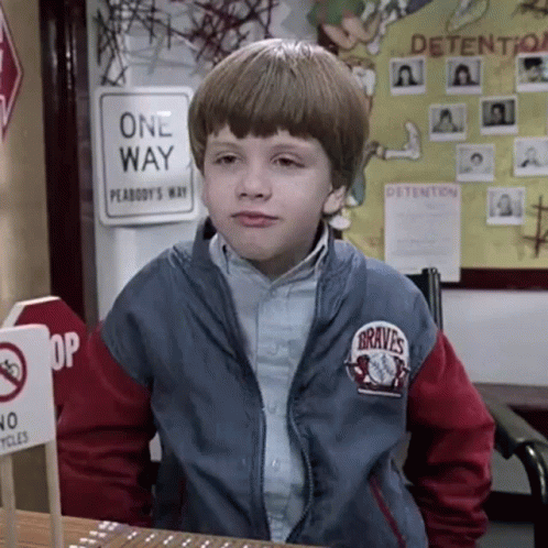 A Young Boy Wearing A Braves Jacket Is Sitting At A Desk In Front Of A One Way Sign . GIF