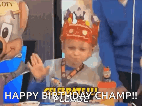A Young Boy Wearing A Crown Is Sitting At A Table With A Chuck E Cheese Mascot . GIF