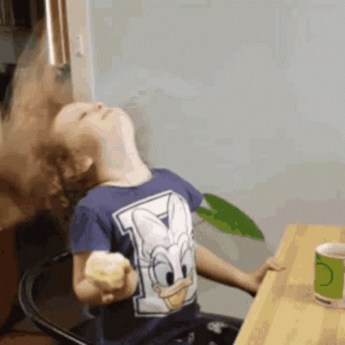 A Young Boy Wearing A Donald Duck Shirt Is Sitting At A Table GIF