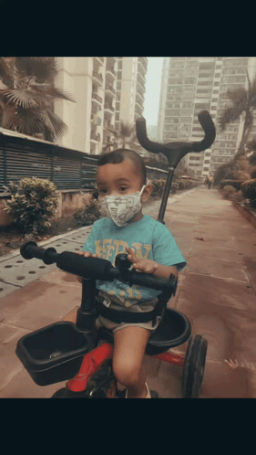 A Young Boy Wearing A Face Mask Is Riding A Tricycle GIF