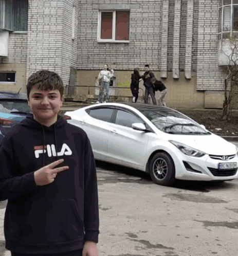 A Young Boy Wearing A Fila Sweatshirt Stands In Front Of A White Car GIF