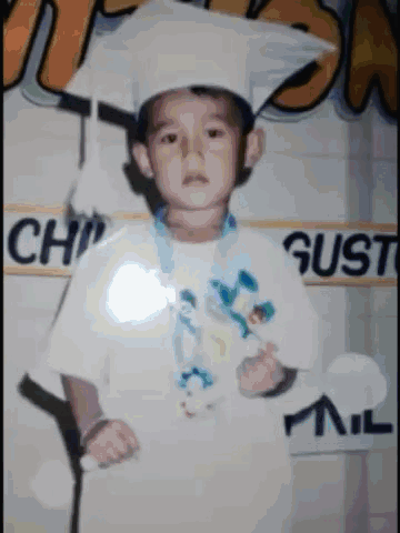 A Young Boy Wearing A Graduation Cap And Gown Poses For A Photo GIF