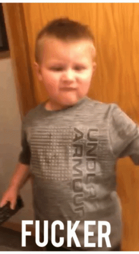 A Young Boy Wearing A Gray Under Armour Shirt Is Standing In Front Of A Wooden Door . GIF
