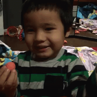 A Young Boy Wearing A Green And Black Striped Shirt Is Holding A Red Ball GIF