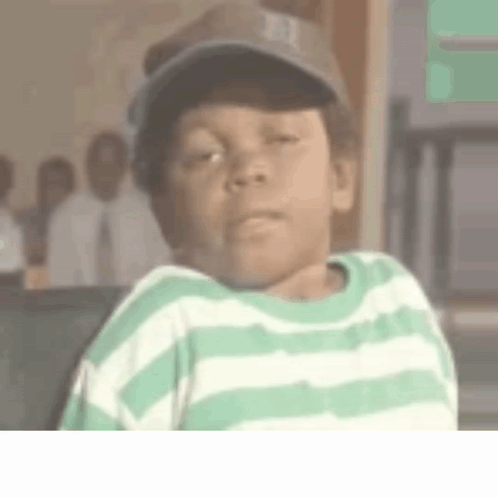 A Young Boy Wearing A Green And White Striped Shirt And A Baseball Cap Is Making A Funny Face . GIF