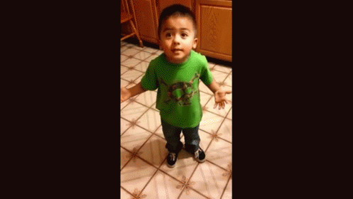 A Young Boy Wearing A Green Shirt Is Standing On A Tiled Floor . GIF