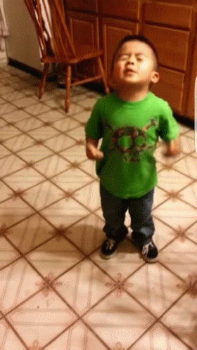 A Young Boy Wearing A Green Shirt With A Skull On It Stands On A Tiled Floor GIF