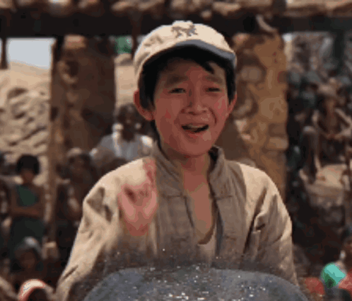 A Young Boy Wearing A Hat Is Standing In Front Of A Group Of People And Smiling . GIF