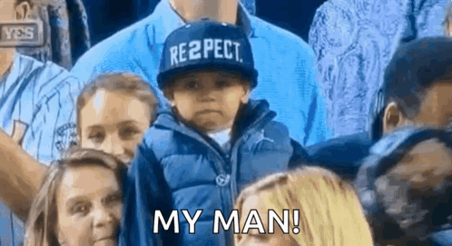 A Young Boy Wearing A Hat That Says Respect Is Sitting In A Crowd . GIF