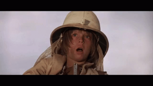 A Young Boy Wearing A Helmet And A Trench Coat Is Looking At The Camera . GIF