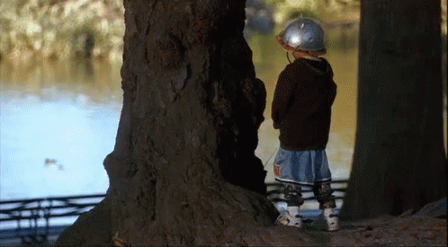 A Young Boy Wearing A Helmet Is Standing Next To A Tree In The Woods GIF