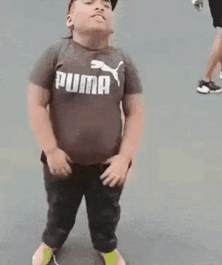 A Young Boy Wearing A Puma T-Shirt And A Hat Is Standing On A Sidewalk . GIF