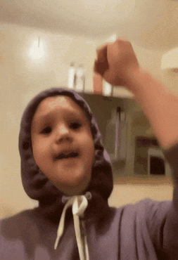 A Young Boy Wearing A Purple Hoodie Is Raising His Fist GIF