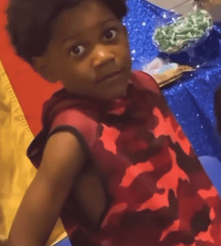 A Young Boy Wearing A Red Camo Shirt Is Looking At The Camera GIF