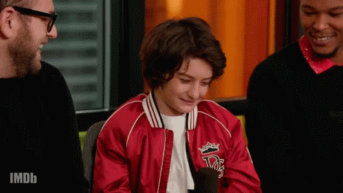 A Young Boy Wearing A Red Jacket With A Crown On It Is Talking Into A Microphone . GIF