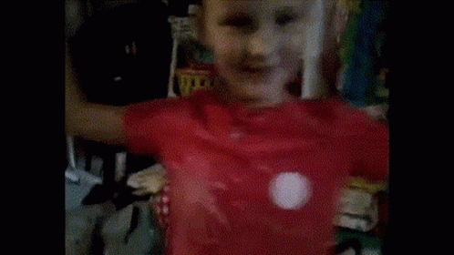 A Young Boy Wearing A Red Shirt Is Standing In Front Of A Shelf GIF