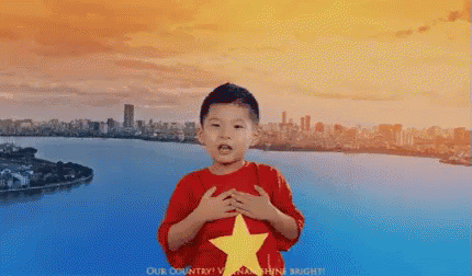 A Young Boy Wearing A Red Shirt With A Yellow Star On It Stands In Front Of A River GIF