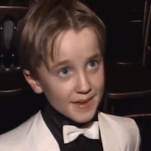 A Young Boy Wearing A Tuxedo And Bow Tie Is Smiling . GIF