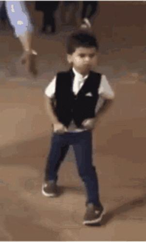 A Young Boy Wearing A Vest And Pants Is Dancing On A Dance Floor . GIF