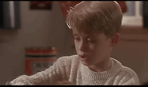 A Young Boy Wearing A White Sweater Is Looking At A Book GIF