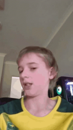 A Young Boy Wearing A Yellow And Green Shirt With The Letter T On It GIF