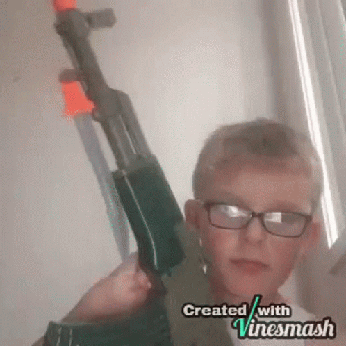 A Young Boy Wearing Glasses Is Holding A Toy Gun In His Hands . GIF