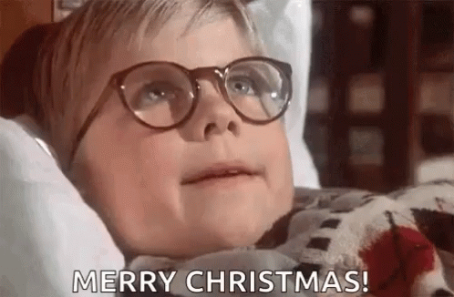 A Young Boy Wearing Glasses Is Laying On A Bed And Saying Merry Christmas . GIF