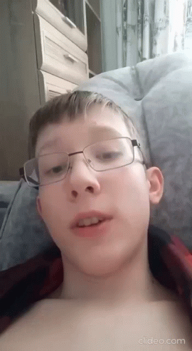 A Young Boy Wearing Glasses Is Laying On A Bed Without A Shirt . GIF