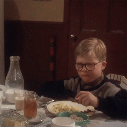 A Young Boy Wearing Glasses Is Sitting At A Table With A Plate Of Food GIF